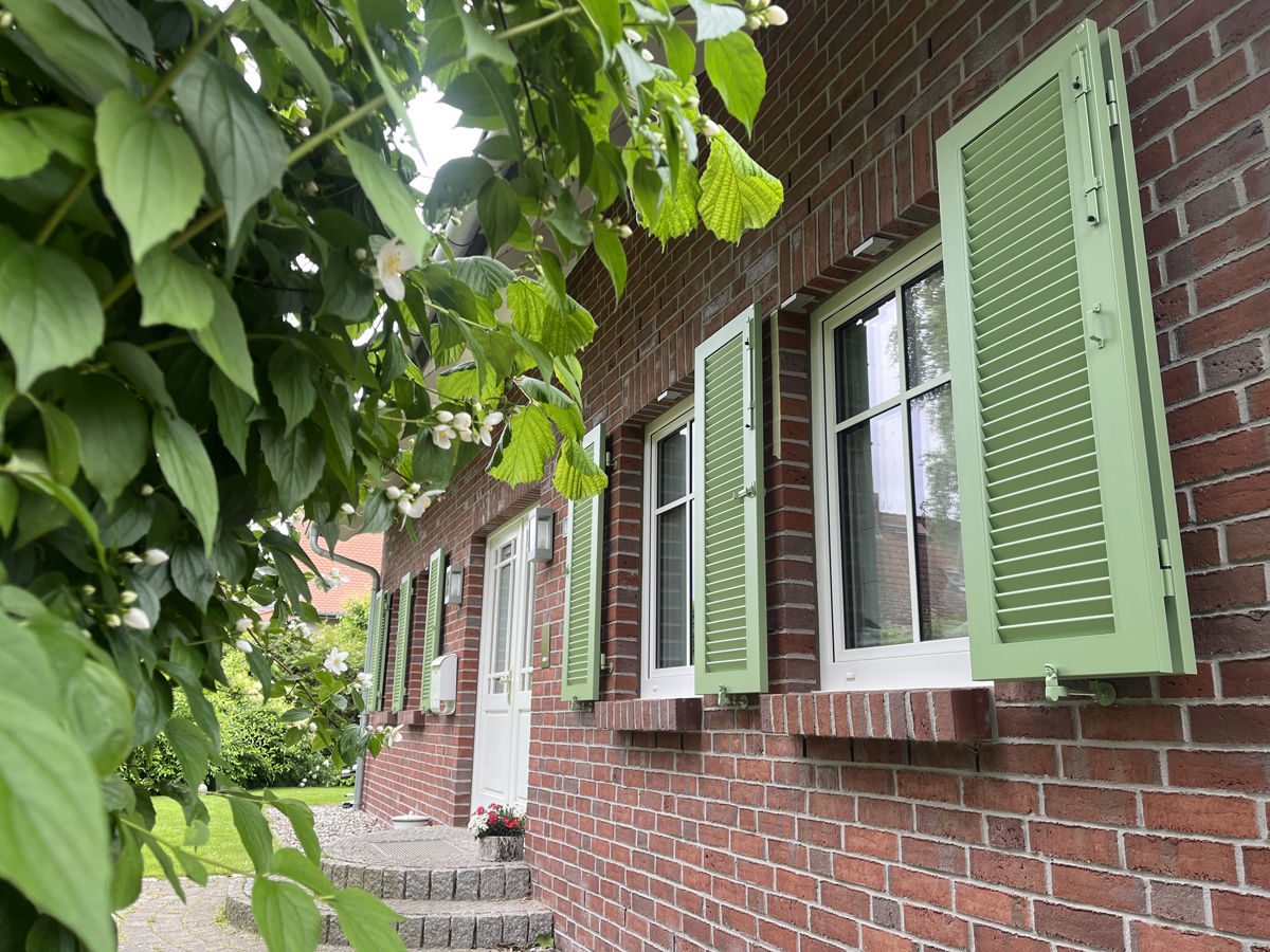 Grüne Klappläden im Farbton Blassgrün an einer Klinkerfassade bei einem Projekt in Greifswald, Mecklenburg-Vorpommern.